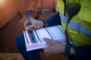 Construction worker filling out a safety form after using hazard identification tools.