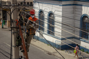 Utility worker fixing wires in a small town as people pass by.