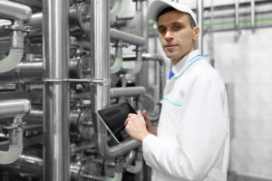 Man in white coat in front of pipes using job safety evaluation tools.