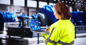 A woman in a safety shirt using OSHA compliance software on an industrial site.