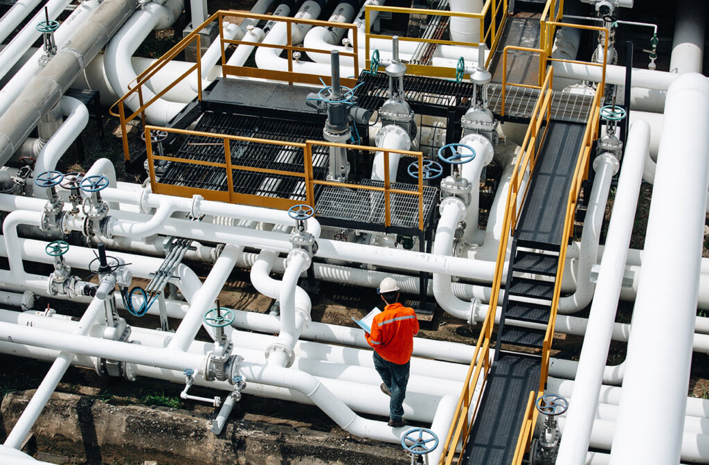 Contractor in orange hi-vis walking a gangway through process piping at a gas plant